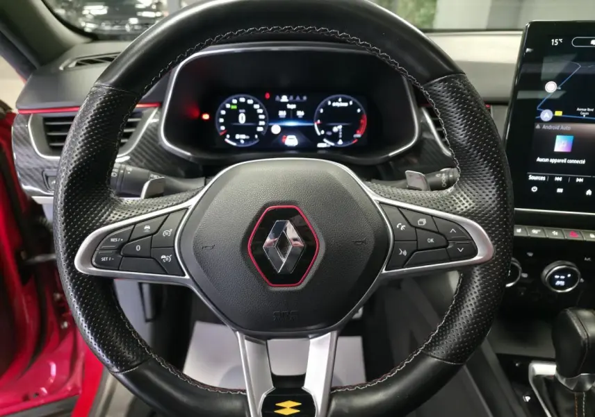 Volant sport en cuir perforé avec logo Renault encadré de rouge, tableau de bord numérique et écran tactile du Renault Arkana R.S. Line rouge.