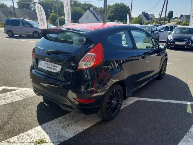 Ford Fiesta noire vue en 3/4 arrière droit avec toit rouge et jantes noires sur parking extérieur.