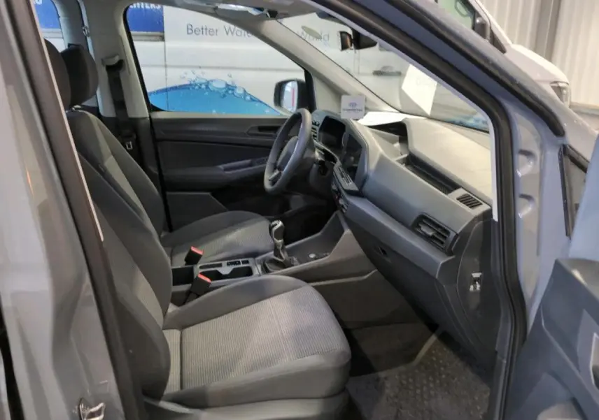 Vue intérieure côté conducteur du Volkswagen Caddy Maxi 2024 gris, montrant sièges et tableau de bord moderne.