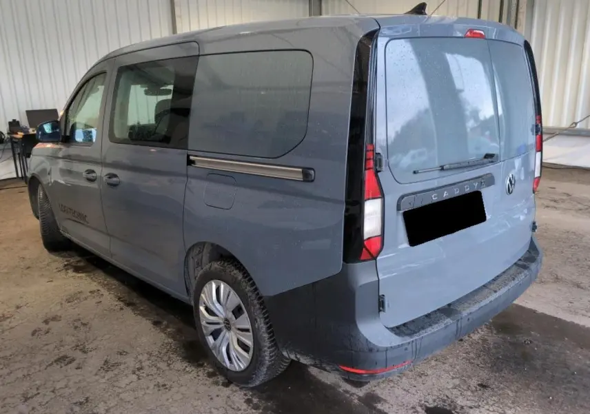 Vue 3/4 arrière droite d'un Volkswagen Caddy Maxi 2024 gris Pure Grey avec portes arrière battantes et vitres teintées.