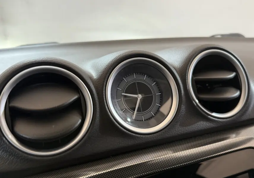 Gros plan sur l'horloge ronde et les aérateurs noirs cerclés d'argent du tableau de bord du Suzuki Vitara noir.