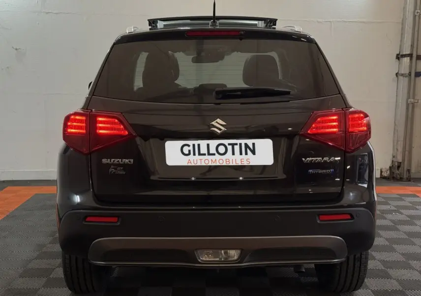 Vue arrière d'un Suzuki Vitara noir 2022 avec feux allumés et badges Hybrid et Vitara visibles.