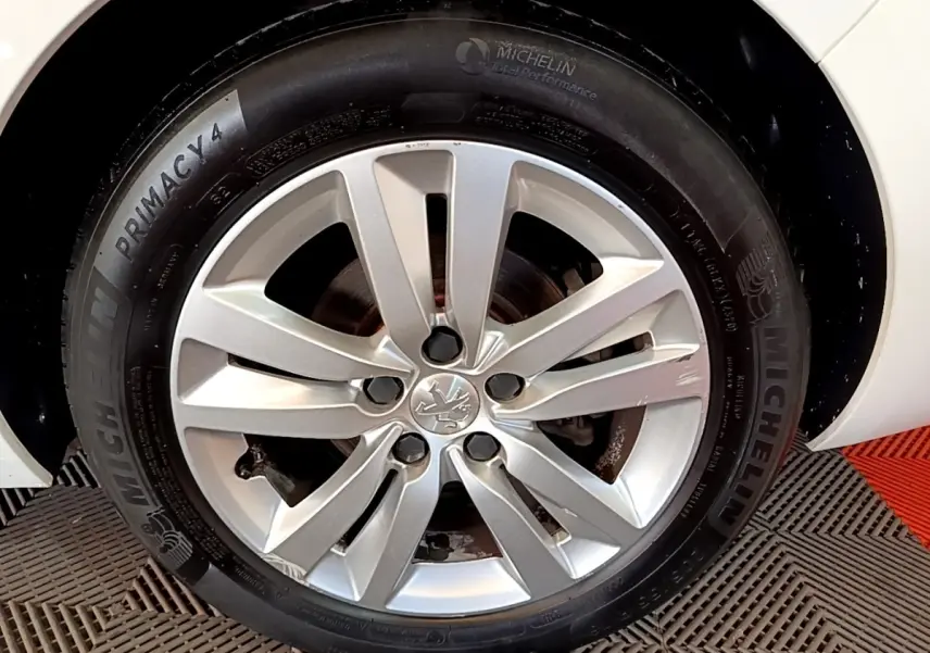 Gros plan sur la roue avant droite d’une Peugeot 308 blanche, jante alliage argent avec logo Peugeot central.