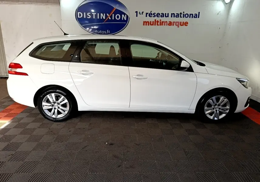 Peugeot 308 break blanc vue de profil côté gauche, avec jantes alliage et rétroviseurs blancs dans un showroom.