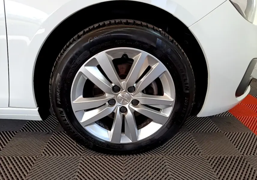Gros plan sur la roue avant droite d’une Peugeot 308 blanche, jante alliage argentée et pneu Michelin visible.