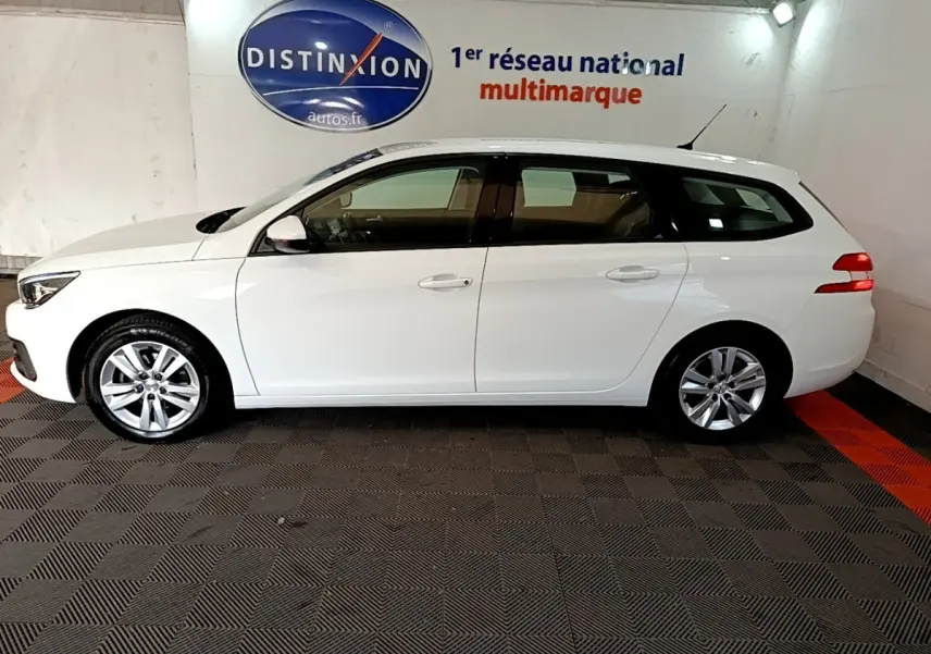 Peugeot 308 break blanc vue de profil côté gauche dans un showroom avec sol à damier noir et rouge.