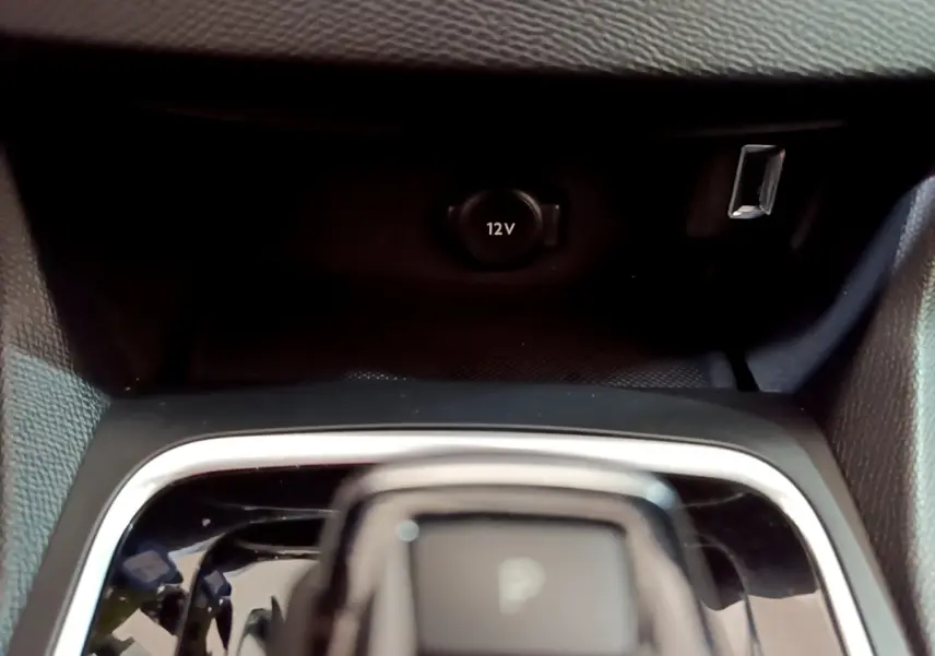 Gros plan sur la console centrale noire de la Peugeot 308 blanche, avec prise 12V et port USB visibles.
