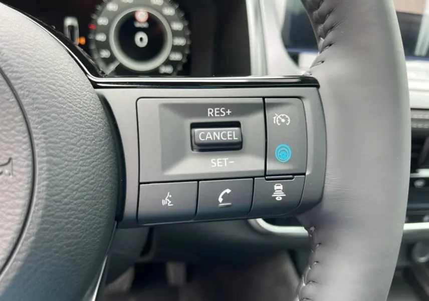 Gros plan sur les commandes du volant cuir gris du Nissan Qashqai E-POWER 205 Tekna Plus, avec boutons multifonctions.