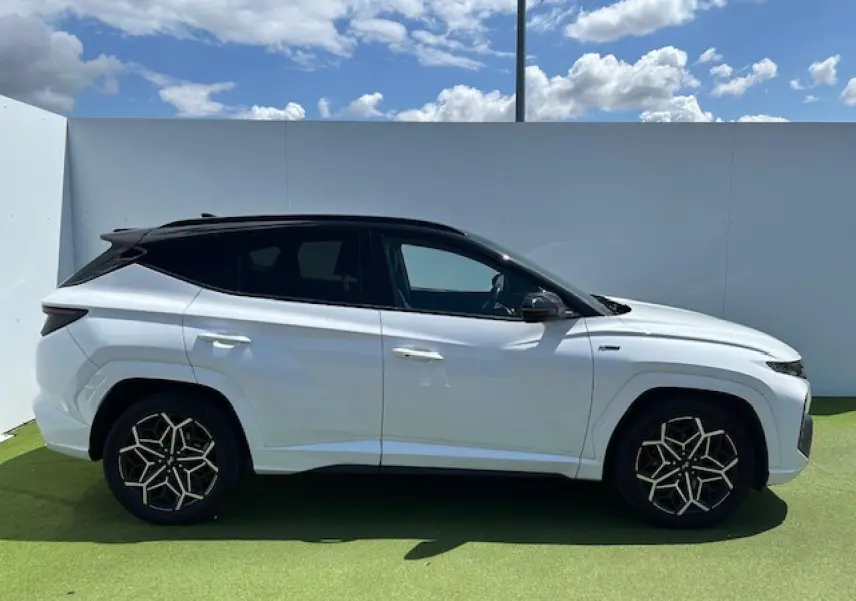 Vue latérale droite du Hyundai Tucson blanc polaire avec toit noir et jantes au design géométrique.