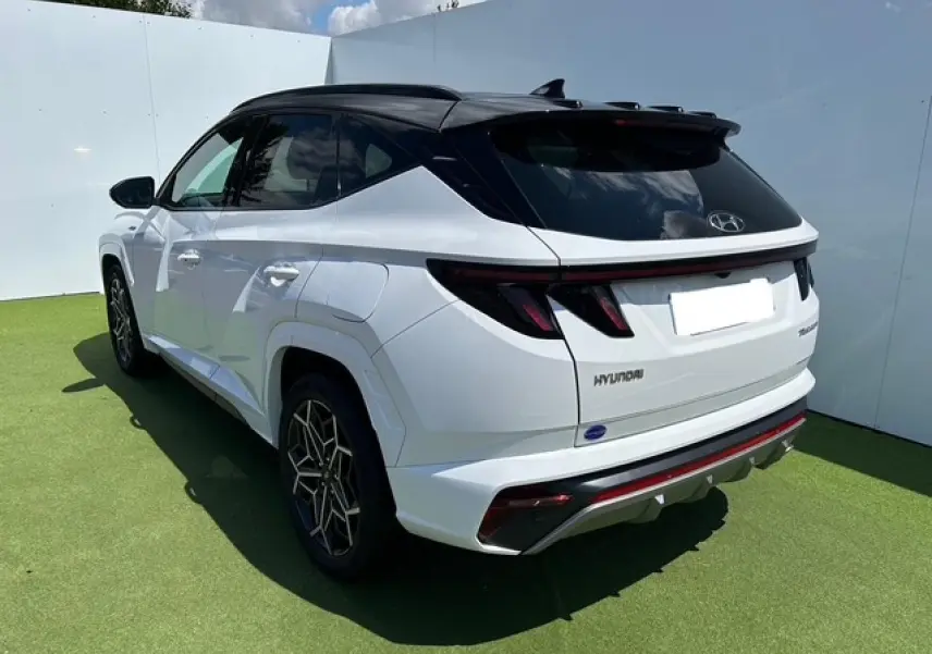 Vue 3/4 arrière droite du Hyundai Tucson blanc polaire avec toit noir et détails N-LINE visibles sur pare-chocs et jantes.