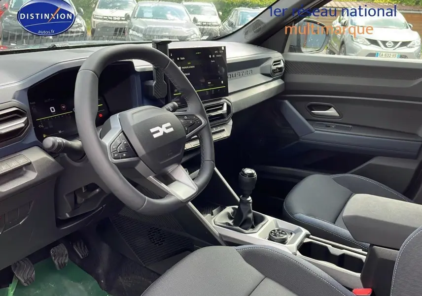 Intérieur du Dacia Duster 2025 montrant le poste de conduite avec volant multifonction, écran tactile et levier de vitesse manuel.