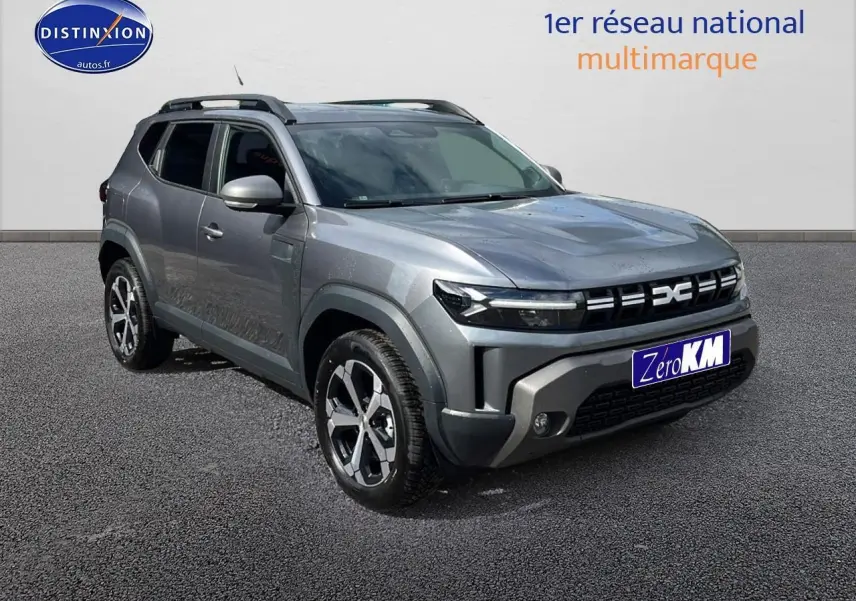 Dacia Duster gris schiste en 3/4 avant droit, avec barres de toit et jantes alu distinctives.