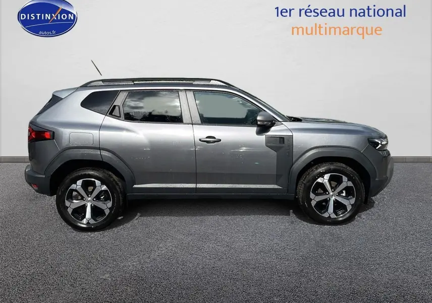 Profil droit du Dacia Duster gris schiste 2025 avec jantes alu et barres de toit visibles sur fond neutre.