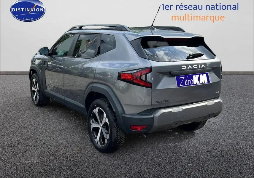 Vue 3/4 arrière droite du Dacia Duster gris schiste 2025 avec jantes alu et barres de toit noires.