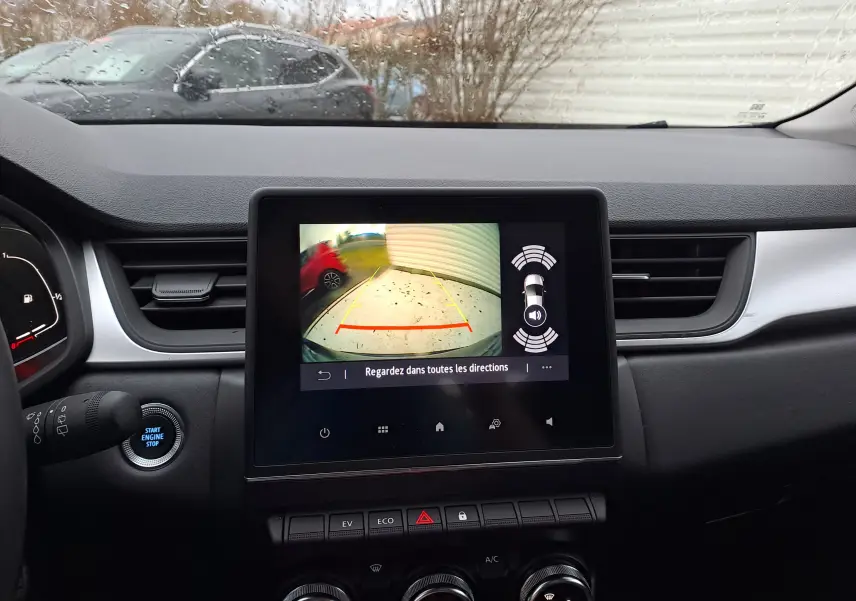 Vue intérieure du tableau de bord du Renault Captur gris cassiopée, avec écran de caméra de recul et commandes climatisation visibles.