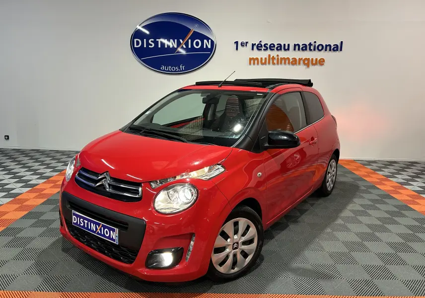 Citroën C1 rouge vue 3/4 avant droit, toit ouvrant Airscape ouvert, dans un showroom avec sol gris et orange.