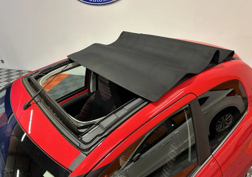 Vue plongeante sur l'avant gauche d'une Citroën C1 rouge 3 portes avec toit ouvrant en toile partiellement déployé.