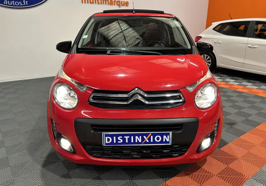 Vue frontale d'une Citroën C1 rouge 2019 avec phares et feux antibrouillard allumés en intérieur showroom.