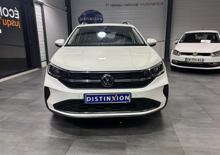 Vue avant d'un Volkswagen Taigo blanc 2023 avec calandre noire et logo VW central dans un showroom.