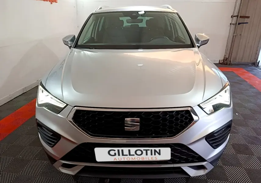 Vue avant d'un SEAT Ateca gris clair avec calandre hexagonale noire et phares LED allumés dans un garage.