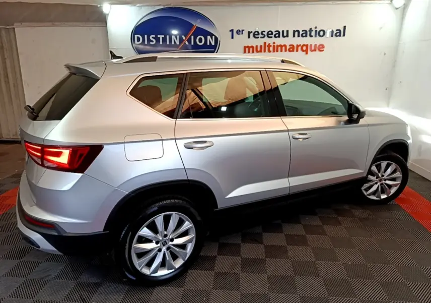 Vue 3/4 arrière droite d'un SEAT Ateca gris clair 2022 avec jantes alliage et feux LED allumés en intérieur.