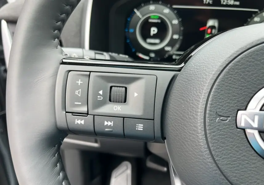 Gros plan sur les commandes multimédia à gauche du volant cuir gris du Nissan Qashqai E-Power 205 Tekna Plus.