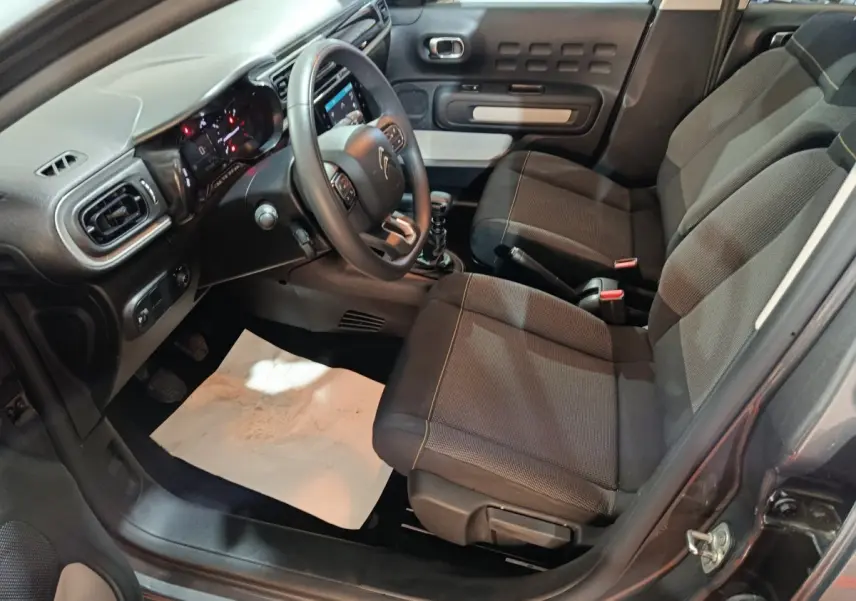 Vue intérieure côté conducteur de la Citroën C3 gris foncé 2024, montrant sièges tissu et tableau de bord avec volant multifonctions.