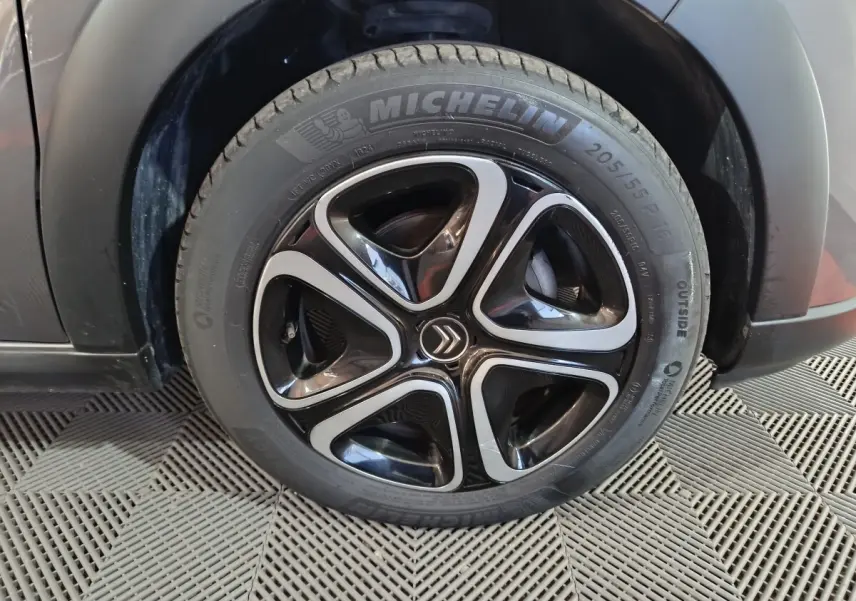 Gros plan sur la roue avant droite d'une Citroën C3 gris foncé avec jante noire et argentée au design moderne.