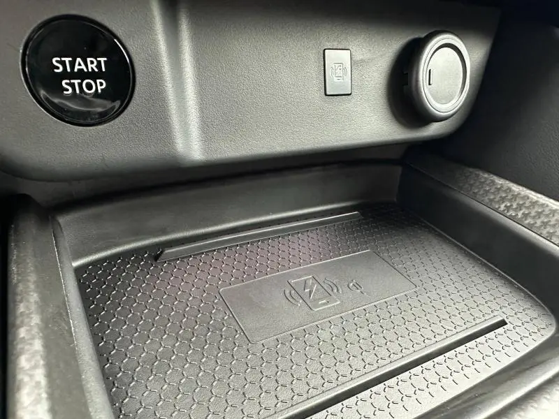Détail intérieur du Nissan Qashqai Hybrid e-POWER 2025 montrant le bouton Start/Stop et un espace de recharge sans fil avec symbole Qi.