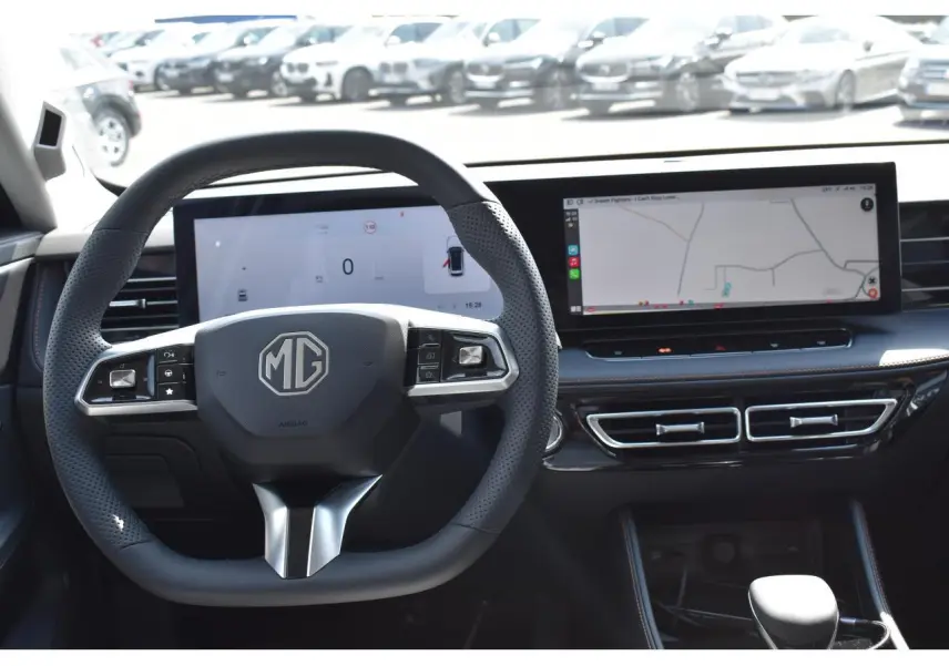 Vue intérieure centrée sur le volant MG et le tableau de bord numérique avec écran tactile et navigation affichée.