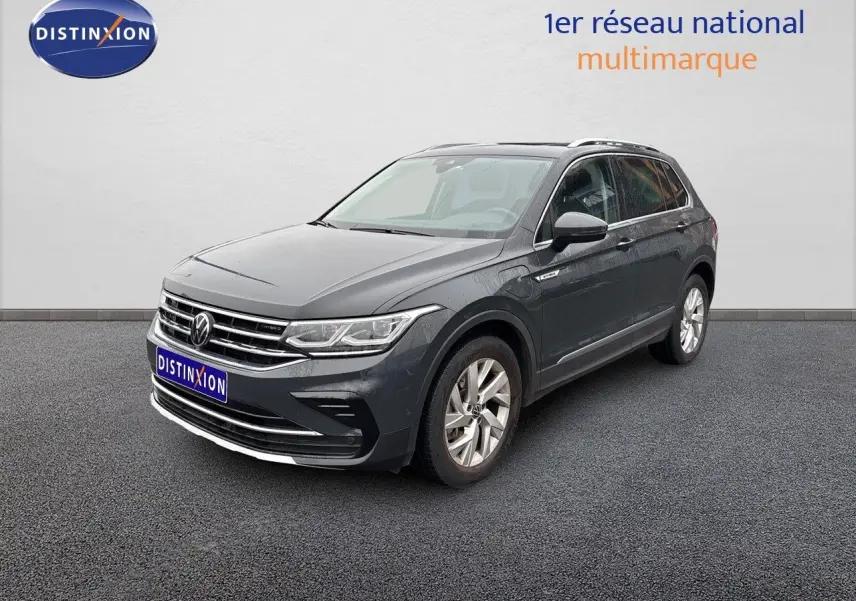 Volkswagen Tiguan 1.4 E-Hybrid gris lunaire en 3/4 avant droit sur sol gris devant un mur blanc.