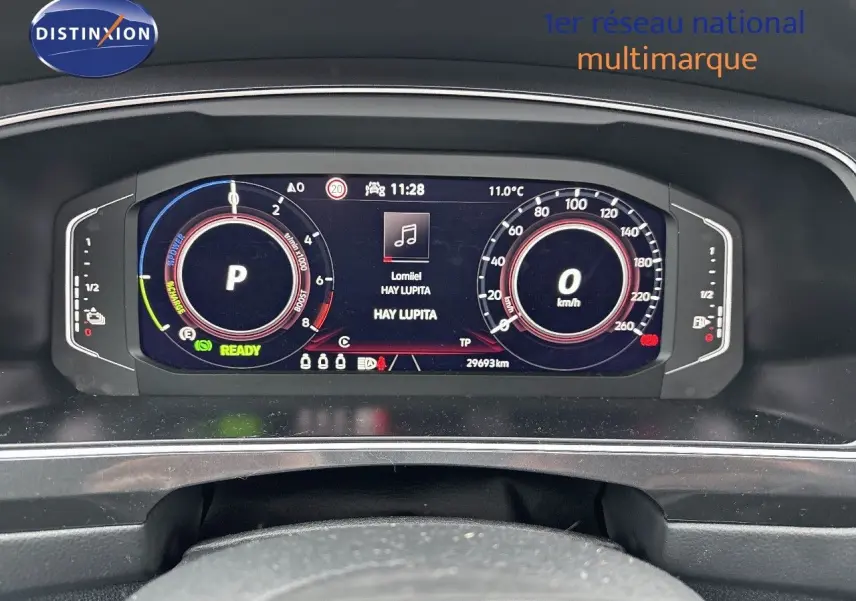 Tableau de bord numérique du Volkswagen Tiguan 1.4 E-HYBRID 245CH, affichant vitesse, mode parking et musique en cours.