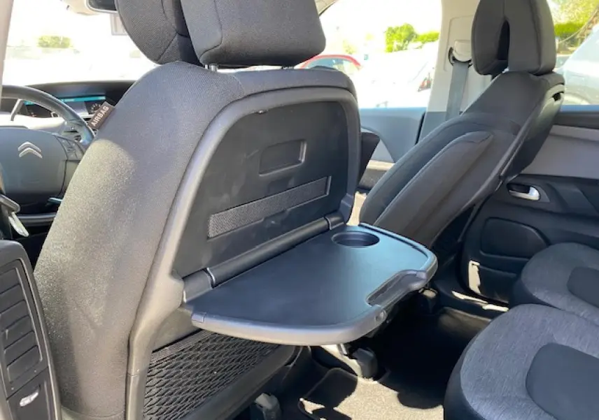 Vue intérieure arrière droite du Citroën C4 Picasso 2016 gris Shark, tablette rabattable avec porte-gobelet sur siège avant.