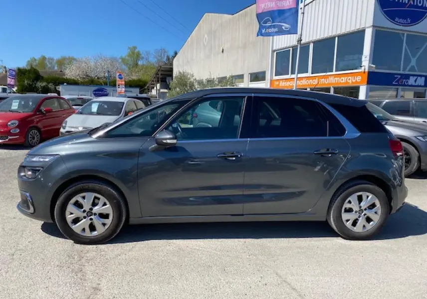 Profil latéral droit d'une Citroën C4 Picasso gris shark garée en extérieur devant un concessionnaire multimarque.