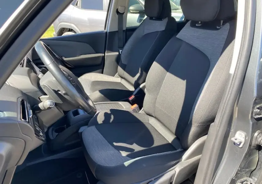 Vue intérieure côté conducteur de la Citroën C4 Picasso gris shark, sièges tissu bicolore noir et gris, volant cuir visible.
