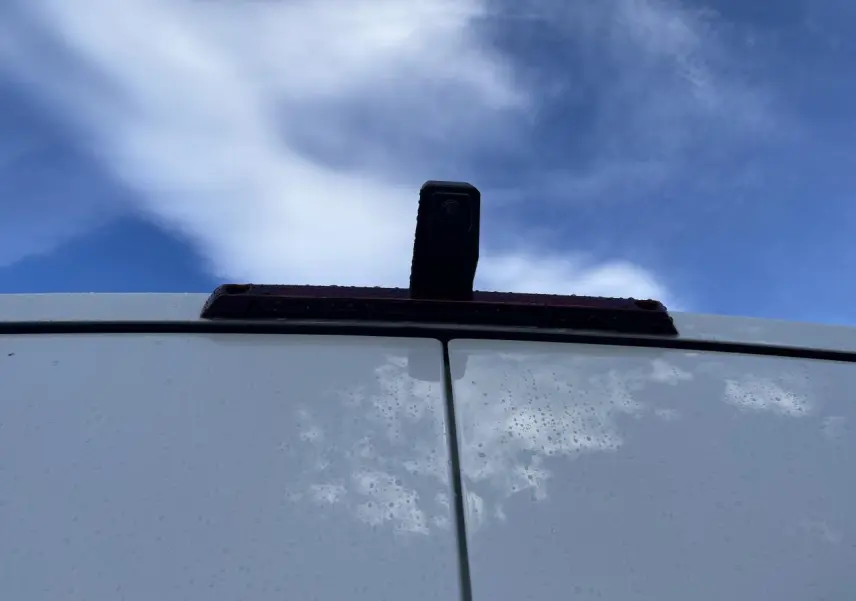 Vue rapprochée de la caméra de recul sur la porte arrière blanche du Renault Master 2025 sous un ciel bleu.