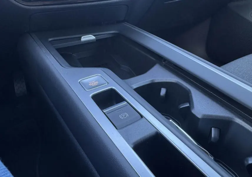 Gros plan sur la console centrale noire de la Volkswagen Passat SW 2024, avec bouton start/stop et frein électronique.