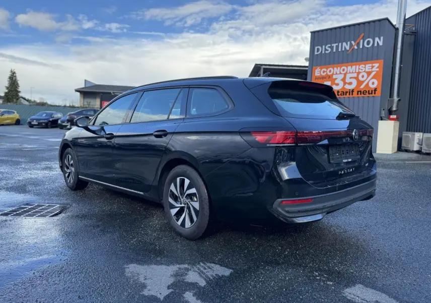 Volkswagen Passat SW noire vue 3/4 arrière droit sur parking humide avec jantes alliage et feux LED.