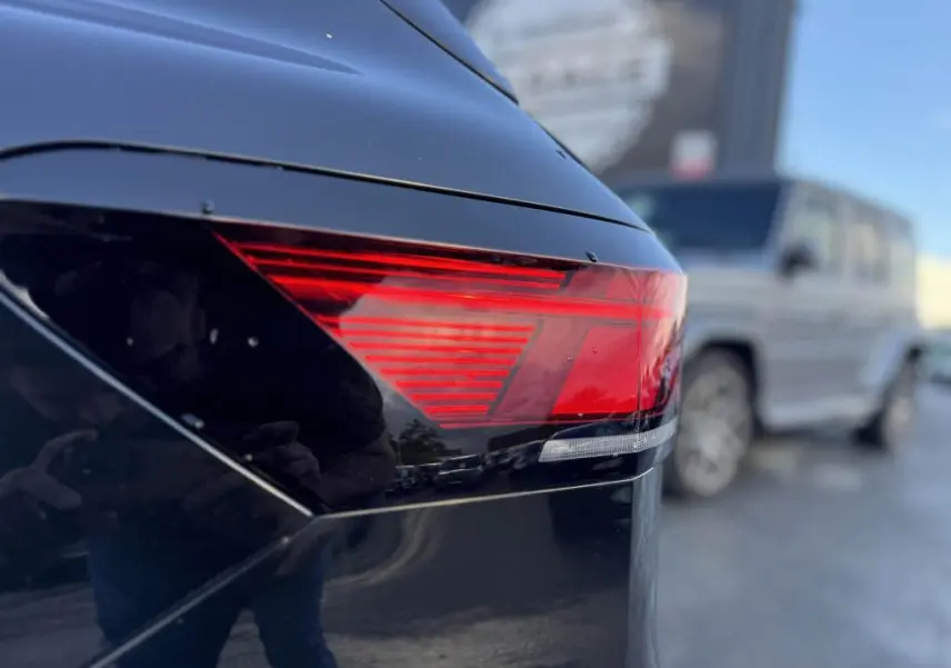 Gros plan sur le feu arrière droit rouge d'une Volkswagen Passat SW noire, finition Life Plus, avec reflet flou d'un autre véhicule en arrière-plan.