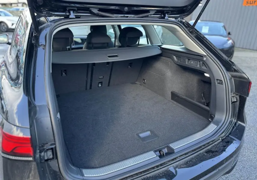 Coffre ouvert vu de l'arrière d'une Volkswagen Passat SW noire 2024, montrant un espace de chargement spacieux et bien fini.