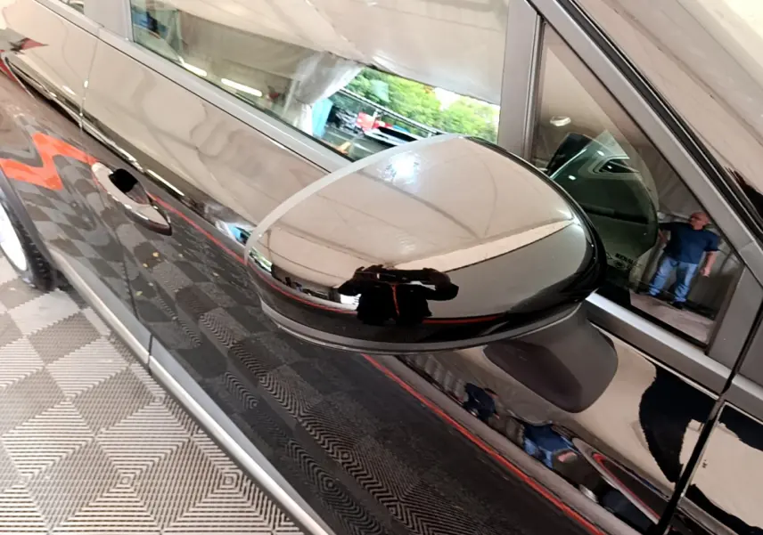 Gros plan sur le rétroviseur côté gauche d'un Renault Captur Business noir brillant, reflet d'un homme visible sur la carrosserie.