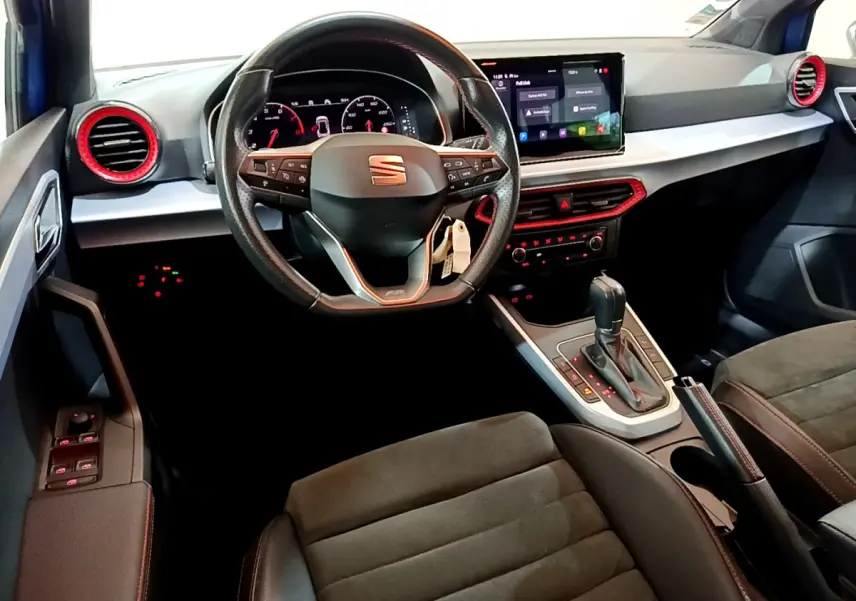 Intérieur vue conducteur du SEAT Arona bleu, volant cuir, tableau de bord digital et aérateurs rouges contrastants.