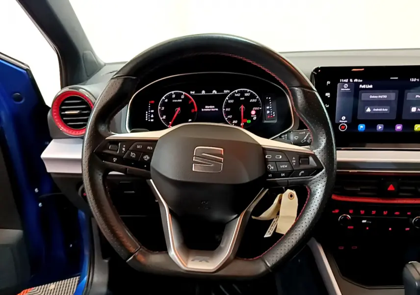 Vue intérieure centrée sur le volant cuir perforé avec surpiqûres rouges du SEAT Arona bleu 2022, tableau de bord digital visible.