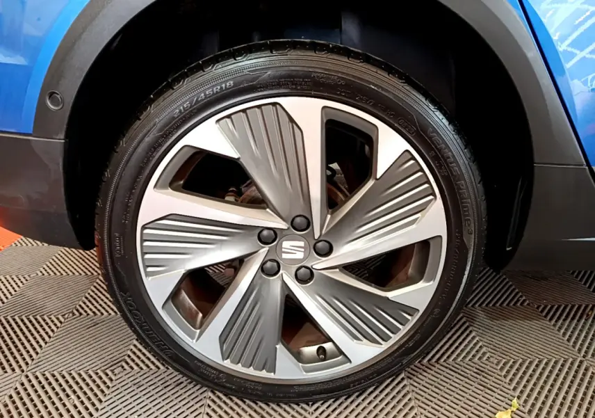 Gros plan sur la roue avant droite d’un SEAT Arona bleu, avec jante alliage au design moderne et logo central.