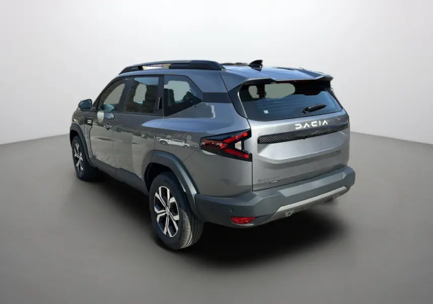 Vue 3/4 arrière droite du Dacia Bigster gris schiste avec barres de toit et jantes alu 17 pouces visibles.