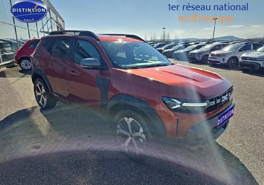 Dacia Duster brun terracotta vu en 3/4 avant droit avec barres de toit et jantes alu distinctives.