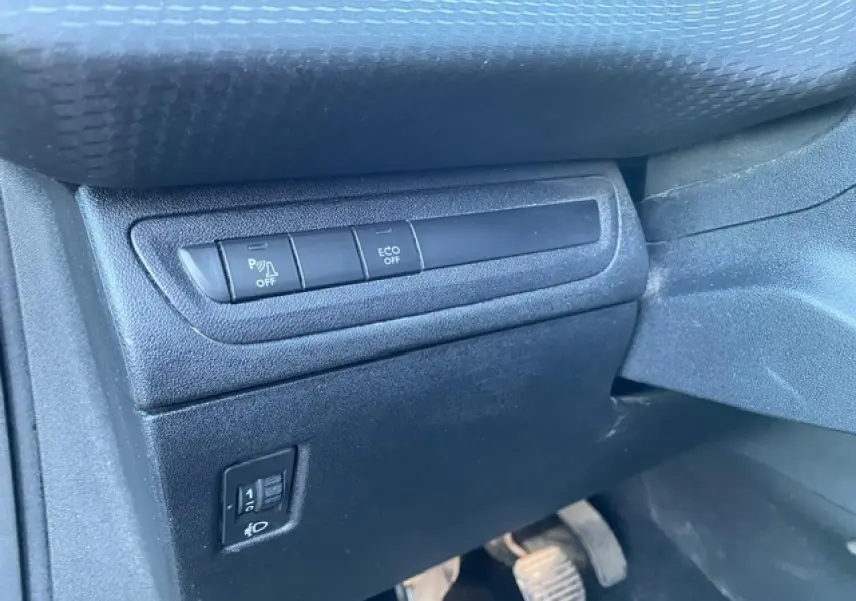 Vue rapprochée des commandes d'aide au stationnement et d'économie d'énergie sur le tableau de bord côté conducteur d'une Peugeot 2008 noire.