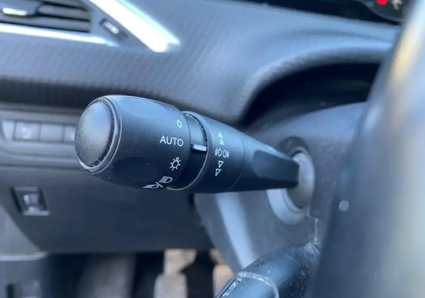 Gros plan sur la commande d'éclairage à gauche du volant dans l'habitacle d'un Peugeot 2008 noir de 2019.