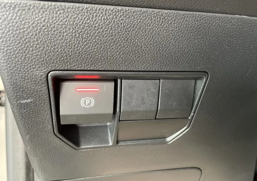Gros plan sur le bouton de frein de stationnement électrique allumé dans l'habitacle du Dacia Duster beige.