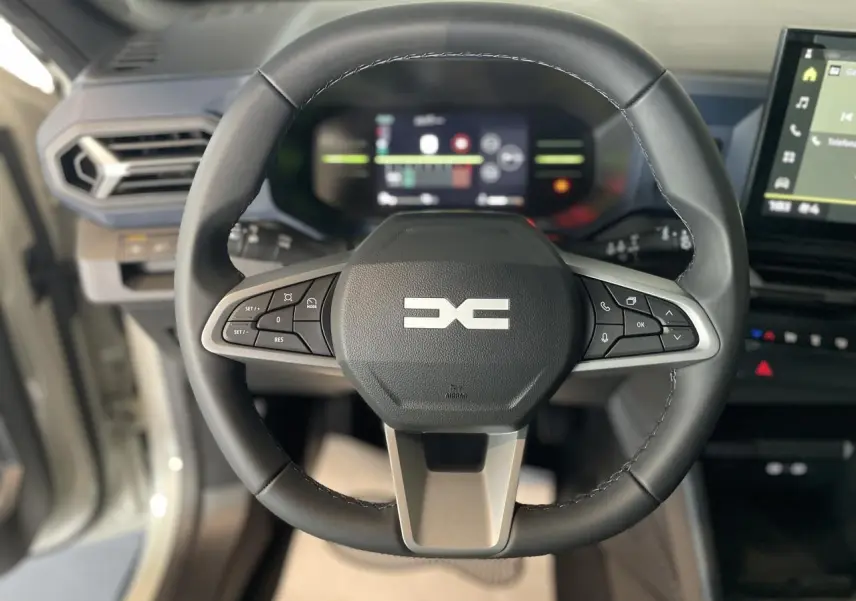 Vue rapprochée du volant noir du Dacia Duster 2025 avec commandes intégrées et tableau de bord digital flou en arrière-plan